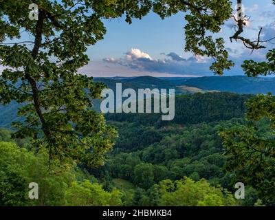 Vista incorniciata da alberi di una campagna montagnosa, lungo la strada di San Giacomo, presa alla fine del pomeriggio a Saint-Privat-d'Allier, Francia Foto Stock
