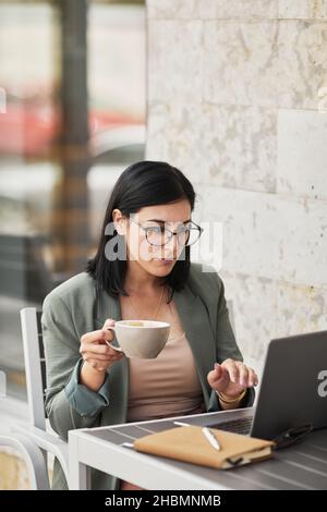 Ritratto verticale di giovane donna d'affari di successo che usa un computer portatile al bar all'aperto Foto Stock