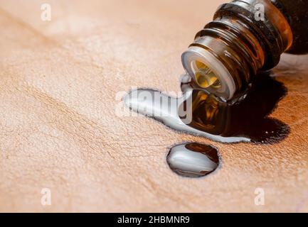 bottiglia d'olio essenziale che si spillano è contenuto su una superficie di pelle marrone. Mobili in pelle rovinando macro concetto. Foto Stock