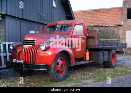 Vecchio rosso Chevrolet pick Up dal 1942 con piattaforma di carico in legno e registrazione olandese, in piedi di fronte a un capannone Foto Stock