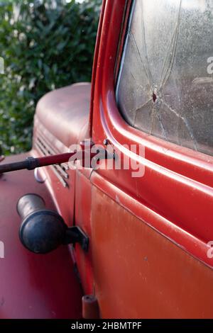 Vista laterale del vecchio pick up rosso della metà del 20th secolo con un buco proiettile e crepa nella porta del finestrino dell'auto. Concentratevi sul foro della pallottola a destra Foto Stock