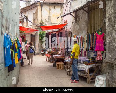 CITTÀ DI PIETRA, ZANZIBAR, TANZANIA - 13 MARZO 2017: Strada stretta con turisti e mercanti Vendita di tessuti colorati a Stone Town, Zanzibar Foto Stock