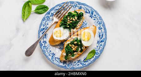 Panini con spinaci fritti, uova e pinoli su sfondo chiaro. Deliziosa colazione sana o snack. Vista dall'alto. Foto Stock