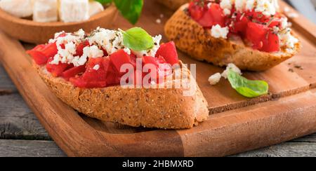 Bruschetta con pomodori, feta e basilico. Tradizionale spuntino greco su sfondo di legno. Messa a fuoco selettiva. Foto Stock