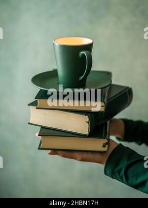 Mani che tengono pochi libri e una tazza di caffè Foto Stock
