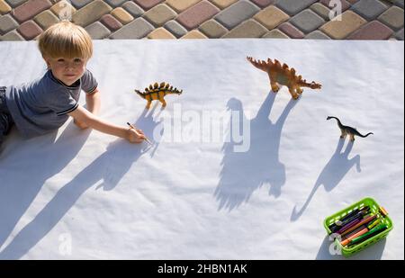 i bambini disegnano con una matita ombre contrastanti dai dinosauri giocattolo, disegnando un preschooler e idee creative per la creatività dei bambini. Attività interessante Foto Stock