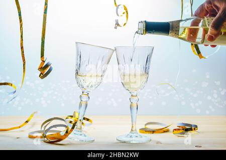 Versando champagne da una bottiglia in due bicchieri per brindare per l'anno nuovo o altre celebrazioni, festive dorate streamers su uno sfondo chiaro, selec Foto Stock