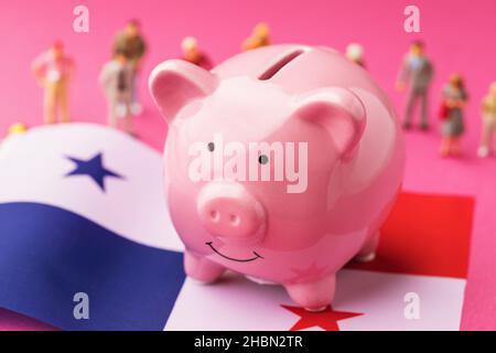 Piggy banca, bandiera di Panama e giocattoli di plastica uomini su uno sfondo colorato, concetto sul tema del reddito della popolazione di Panama Foto Stock