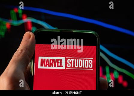 In questa illustrazione della foto, il logo dell'etichetta di produzione cinematografica americana di proprietà di Disney, Marvel Studios, visto su uno smartphone con un grafico di indice di borsa economica sullo sfondo. Foto Stock