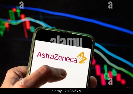 In questa illustrazione della foto il logo della multinazionale britannica-svedese farmaceutica e biotecnologica AstraZeneca è stato visualizzato su uno smartphone con un grafico dell'indice delle borse economiche sullo sfondo. Foto Stock
