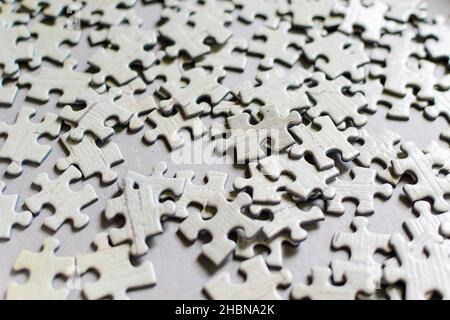 Molti pezzi di puzzle in cartone grigio chiaro testurizzato su un tavolo, attività al coperto nel fine settimana per giocare con i bambini a casa Foto Stock