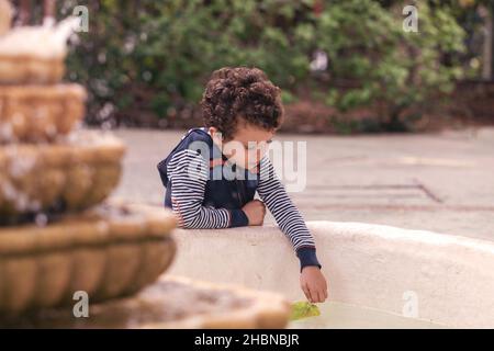 Ragazzo caucasico che gioca con una foglia nell'acqua della fontana Foto Stock