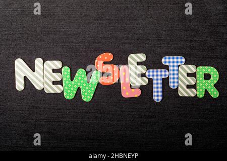 Scheda con Newletter word realizzata con lettere di legno colorate e vivide miste su un materiale tessile nero scuro testurizzato che può essere utilizzato come messaggio Foto Stock