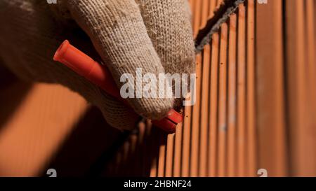 Primo piano delle mani dell'uomo in guanti di protezione martellando un perno nella parete. Concetto di riparazione e ristrutturazione, utensili professionali e per lavoratori. Foto Stock