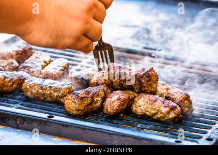 Un primo piano della mano di un uomo che prepara panini di carne sul barbecue Foto Stock