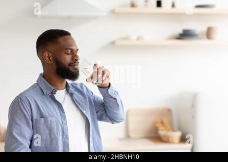 Il giovane maschio afroamericano con occhi chiusi beve acqua dal vetro Foto Stock