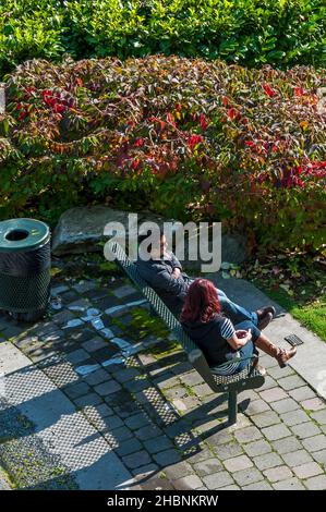 Due persone si siedono su una panchina lungo il Burke Gilman Trail vicino al lato inferiore del ponte Aurora vicino a Fremont, Washington. Foto Stock
