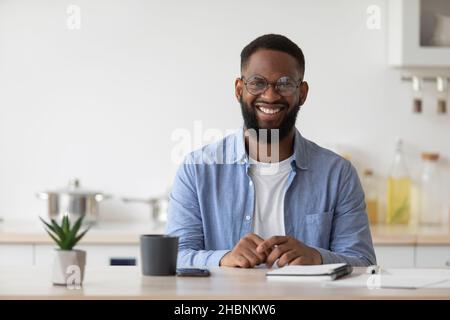 Sorridendo giovane insegnante o studente nero in calici con blocco note e caffè guarda la macchina fotografica Foto Stock