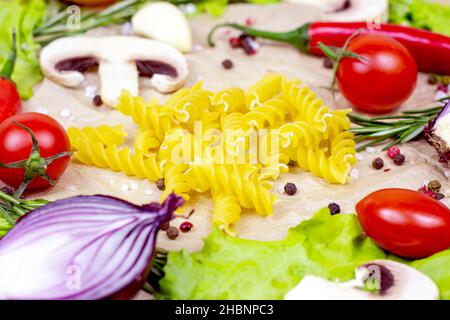 Fusilli gialli e verdure estive brillanti (cipolla, aglio, pomodoro, pepe, rosmarino) e funghi champignon su fondo tavola. Foto Stock