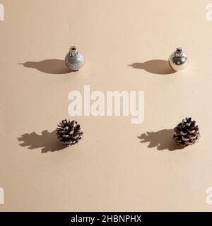Due decorazioni natalizie in argento e due coni su sfondo beige. Scena minimalista Foto Stock