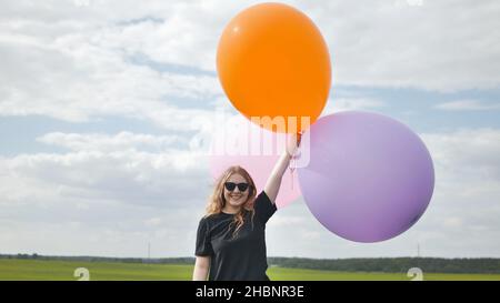 Ragazza felice con grandi palloncini multicolore in posa sul campo. Foto Stock