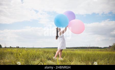 Ragazza felice con grandi palloncini multicolore in posa sul campo. Foto Stock