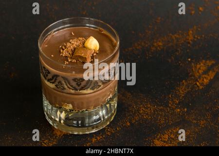 Dessert al budino di cacao con biscotti in calici staylish su nero. Guarnito con noci e cioccolato. Foto Stock