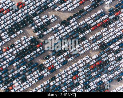 Le nuove autovetture multicolore sono in piedi in file diagonali diritte in un enorme parcheggio sul territorio dello stabilimento, vista aerea Foto Stock