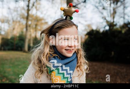 Ragazza sorridente con un cerchietto natalizio che suona all'aperto Foto Stock