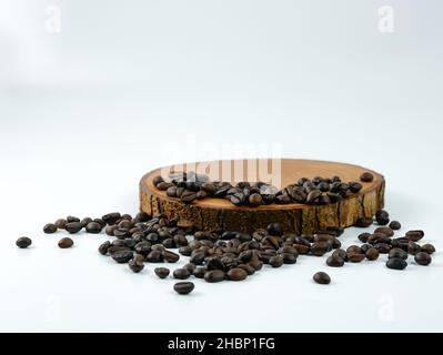 Chicchi di caffè sparsi su un asse di legno rotondo isolato su uno sfondo bianco. Concetto di posizionamento del prodotto. Foto Stock