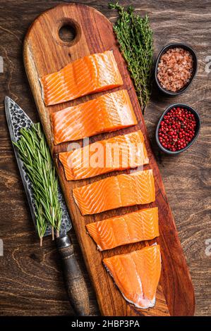 Filetto di salmone affettato, carne di pesce crudo con timo e rosmarino. Sfondo in legno. Vista dall'alto Foto Stock