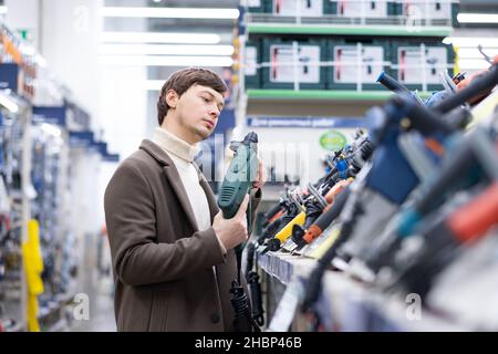 uomo d'affari in un cappotto marrone che sceglie un cacciavite in un negozio di ferramenta per la riparazione Foto Stock