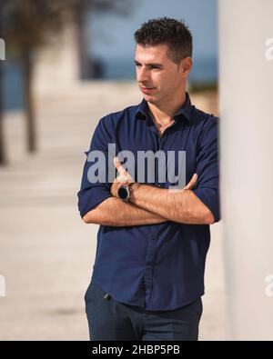 Ritratto di un bel giovane che si pone per una sessione fotografica lungo il fiume tejo a Lisbona, in Portogallo. Elegante architetto freelance che si rilassa da solo Foto Stock