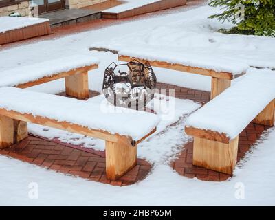 Braciere decorativo intagliato a forma di palla da calcio con figure animali con panchine in legno innevate intorno su una zona innevata Foto Stock