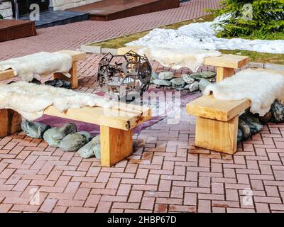 Sochi, Russia - 25 febbraio 2020. Un barbecue decorativo in ferro a forma di palla circondato da panchine di legno ricoperte di pelli animali Foto Stock