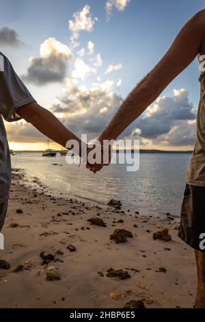 Due uomini che tengono le mani sulla spiaggia durante il tramonto. Concetto di amore per le vacanze. Foto Stock