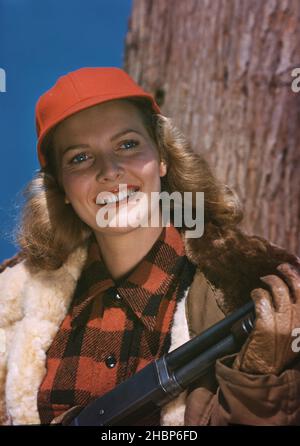 Giovane donna in vestito da caccia e cappello rosso con fucile da caccia Foto Stock