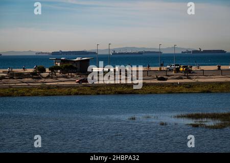La Bolsa Chica Wetlands, con autostrada, spiaggia, ciclisti e in attesa di navi da carico ancorate al largo in attesa di scaricare nel porto di Long Beach. Foto Stock