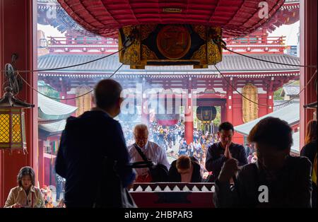 Tokyo, Giappone - 24 ottobre 2019: Persone che pregano all'ingresso della sala principale di fronte alla scatola di offerta (saisen) sotto la grande lanterna rossa (akacho Foto Stock