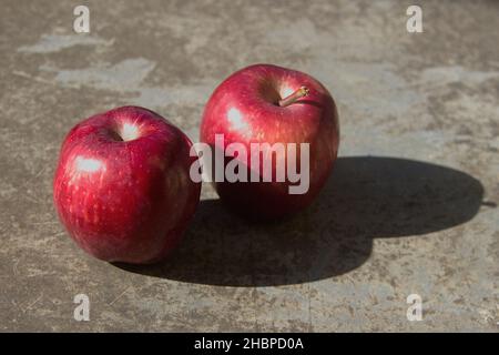 Luce del sole su due mele rosse poste sul pavimento e la loro ombra Foto Stock