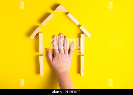 Vista dall'alto della mano del bambino in primo piano blocchi di costruzione che mostrano una casa, casa, capanna di legno Foto Stock