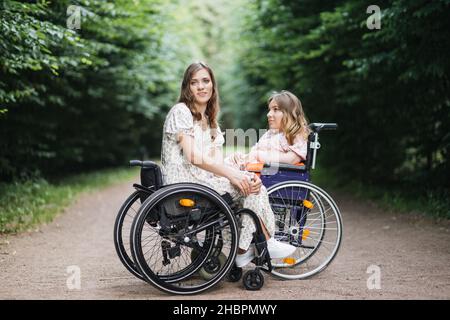 Ritratto di giovani Signore caucasiche in carrozzine seduti di fronte l'uno all'altro nel parco estivo e guardando la macchina fotografica. Concetto di persone con disabilità e stili di vita. Foto Stock