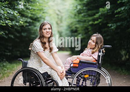 Ritratto di giovani Signore caucasiche in carrozzine seduti di fronte l'uno all'altro nel parco estivo e guardando la macchina fotografica. Concetto di persone con disabilità e stili di vita. Foto Stock