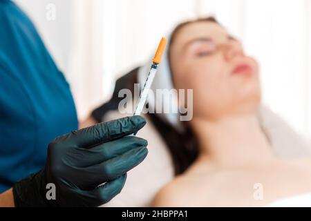 Cosmetologia. Il cosmetologo tiene una siringa con un'iniezione per la procedura di ringiovanimento. Trattamenti beauti in salone. Defocused client sul ba Foto Stock