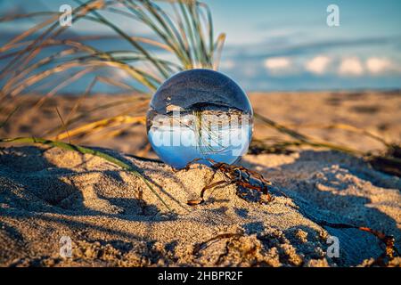 Globo di vetro sulla spiaggia del Mar Baltico in Zingst in cui è raffigurato il paesaggio. Il tramonto crea un'atmosfera calda e luminosa Foto Stock