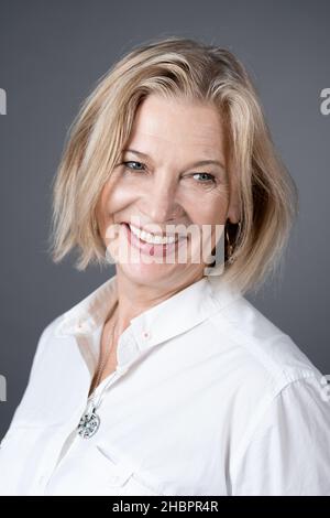 Primo piano di bella donna matura con capelli biondi corti sorridenti mentre si posa alla macchina fotografica Foto Stock