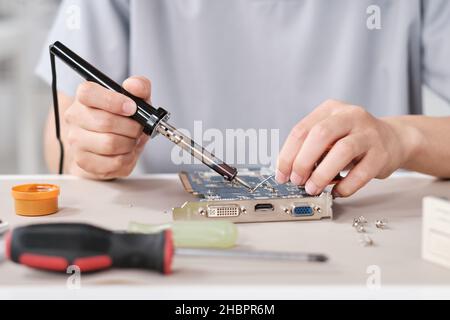 Mani di un giovane tecnico contemporaneo con saldatore che ripara la scheda madre con microchip Foto Stock