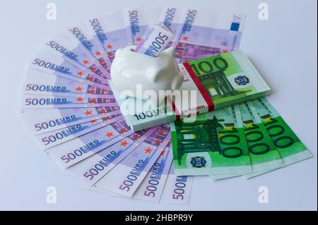 molti euro e dollari bollette sono disposti su uno sfondo viola con un pacchetto di 100 euro e una banca piggy Foto Stock