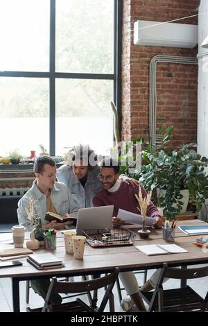 Tre colleghi interculturali che guardano l'esposizione di laptop mentre discutono i punti di lavoro e preparano la presentazione per posto di lavoro Foto Stock