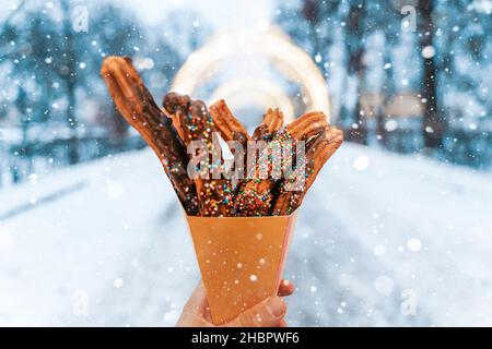 Churros waffle in una mano sul mercato invernale della neve. Churros messicano Street food dessert. Fast food, biscotti della fiera di Natale. Foto di alta qualità Foto Stock